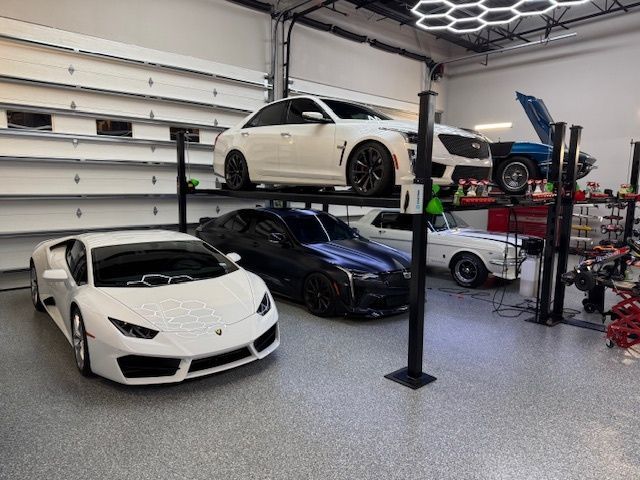 White Lamborghini and other cars in a spacious, well-lit garage with a car lift.