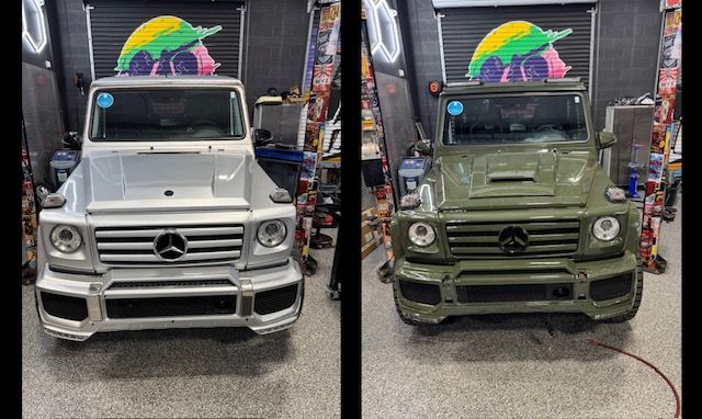 Two Mercedes-Benz G-Wagons, one silver, one olive green, parked side-by-side inside a shop.