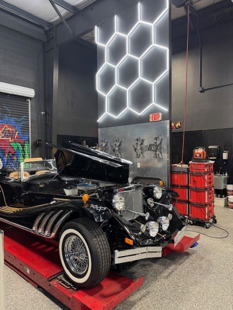 Black classic car being worked on in a modern garage with hexagon lighting and red toolboxes.