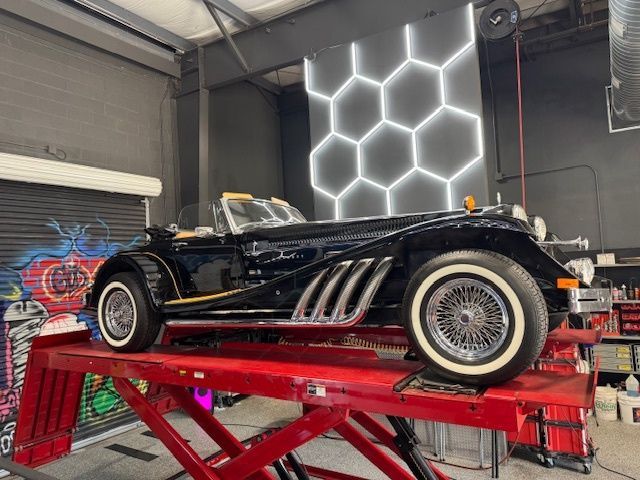 Black vintage car on a red lift in a garage with neon honeycomb wall decor.