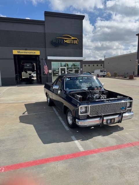 Dark blue Chevy El Camino parked in front of a gray auto repair shop, engine exposed. | Auto Motive