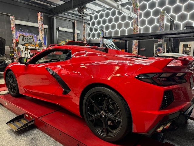Red Chevrolet Corvette on a lift in a garage, black wheels, honeycomb wall.