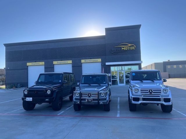 Three Mercedes-Benz G-Wagons parked in front of a gray building with the sun shining behind it.