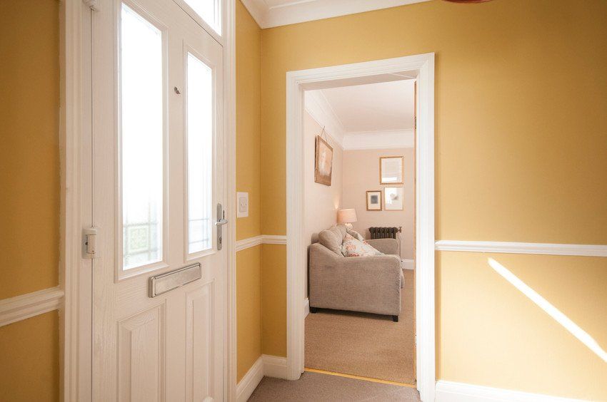 An interior view of a hallway with a front door entrance which leads to the lounge with sofa of a home