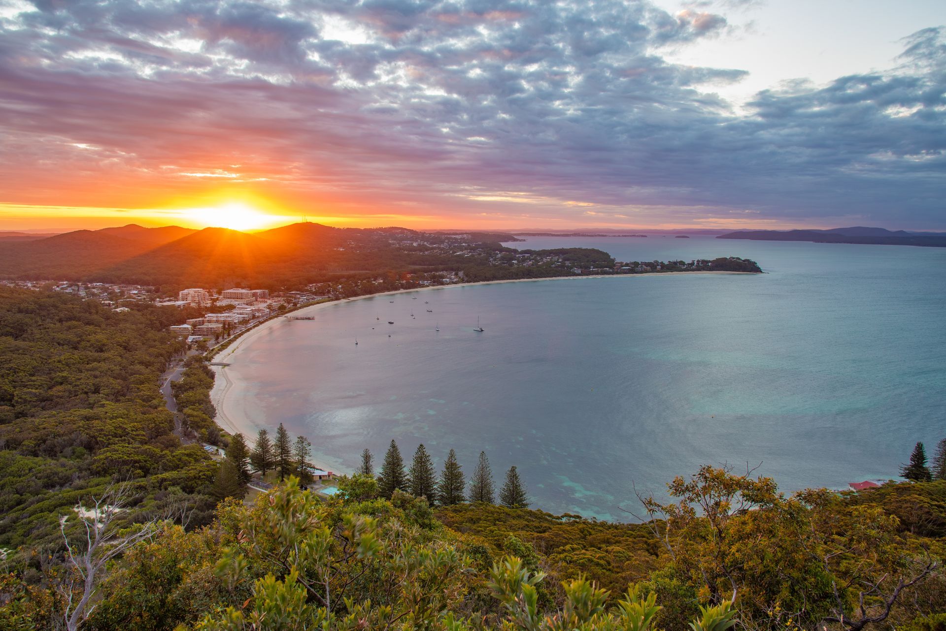 The Sun Is Setting Over A Large Body Of Water Surrounded By Trees — Port Stephens Removals & Storage In Nelson Bay, NSW