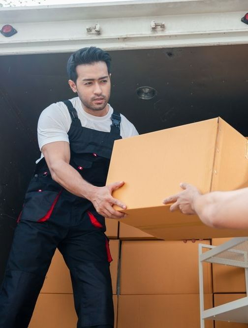 A Man Is Carrying A Cardboard Box Out Of A Truck — Port Stephens Removals & Storage In Stockton, NSW
