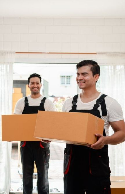 Two Men Are Carrying Cardboard Boxes In A Living Room — Port Stephens Removals & Storage In Stockton, NSW