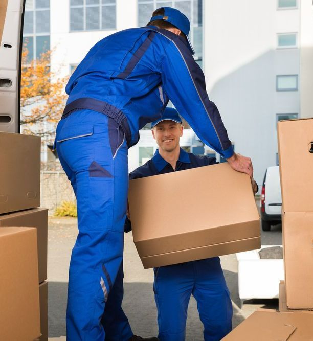 A Man In A Blue Uniform Is Carrying A Cardboard Box — Port Stephens Removals & Storage In Salt Ash, NSW