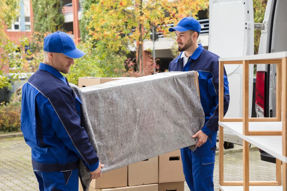 Two Movers Are Carrying A Couch In Front Of A Van — Port Stephens Removals & Storage In Salt Ash, NSW