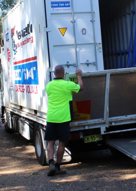 A Man In A Neon Green Shirt Is Loading A Container Into A Moving Truck — Port Stephens Removals & Storage In Anna Bay, NSW