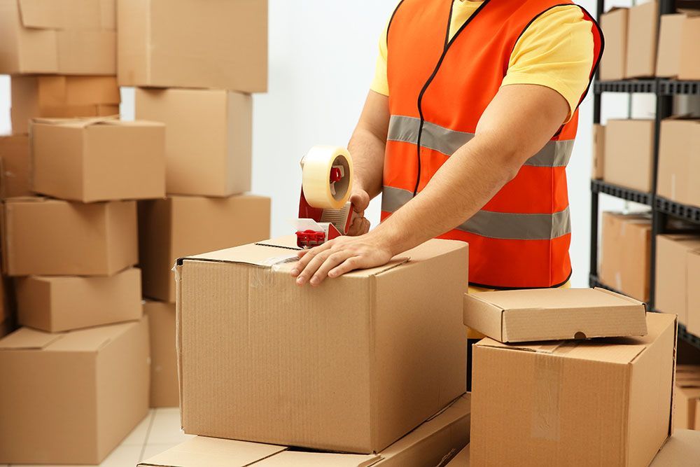 A Man is Taping a Cardboard Box in a Warehouse — Port Stephens Removals & Storage In Salt Ash, NSW