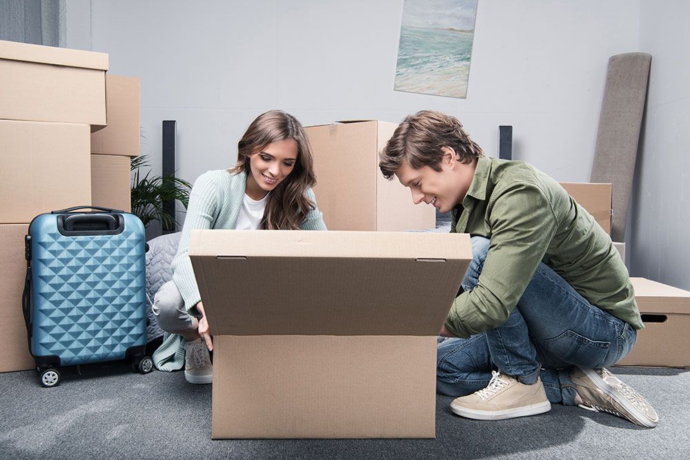 A Man and a Woman Are Opening a Cardboard Box in a Living Room  — Port Stephens Removals & Storage In Salt Ash, NSW