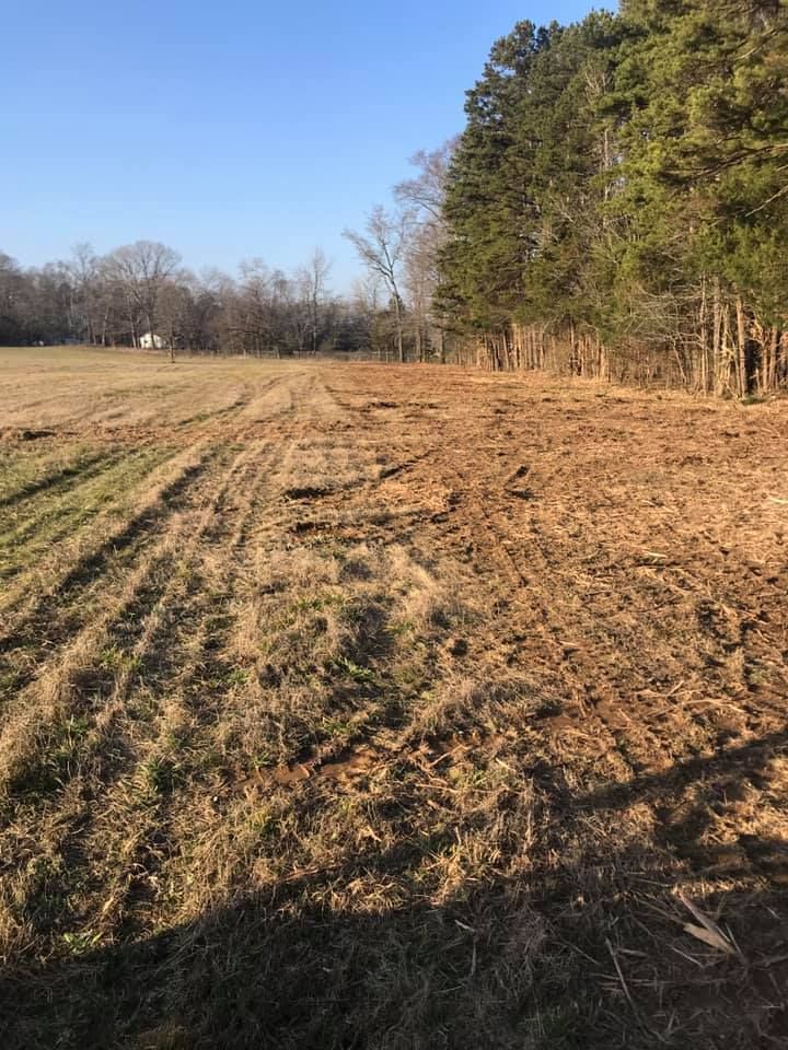 A field with tire tracks and a tree line under a blue sky.