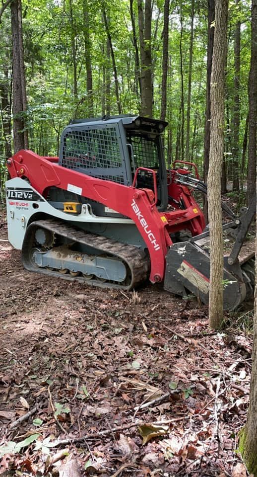 Red and white skid steer in a wooded area, clearing brush.