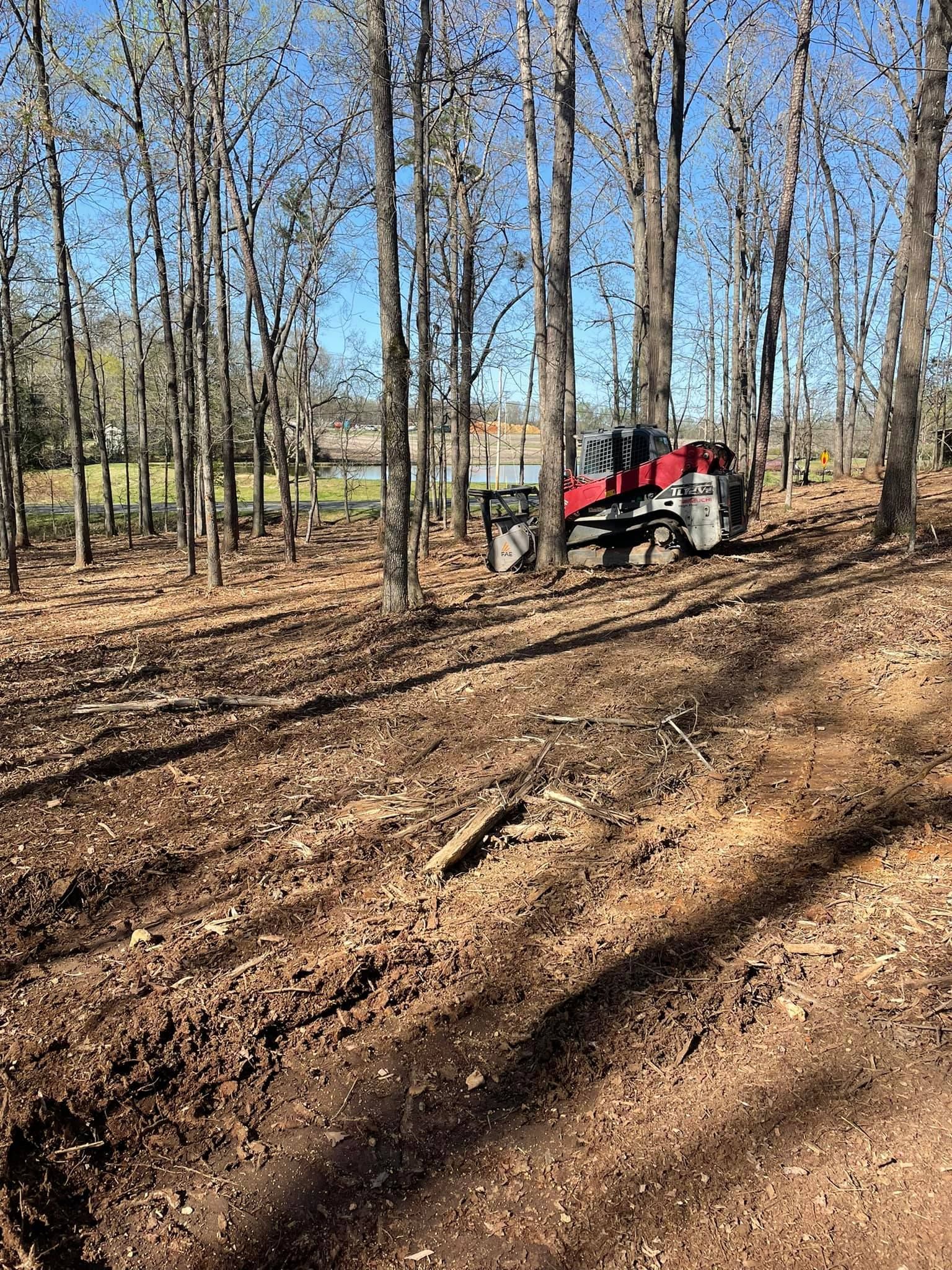 Tractor clearing trees and debris in a wooded area, creating a path.