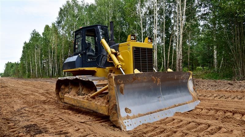 Yellow bulldozer clearing land, forest in the background.