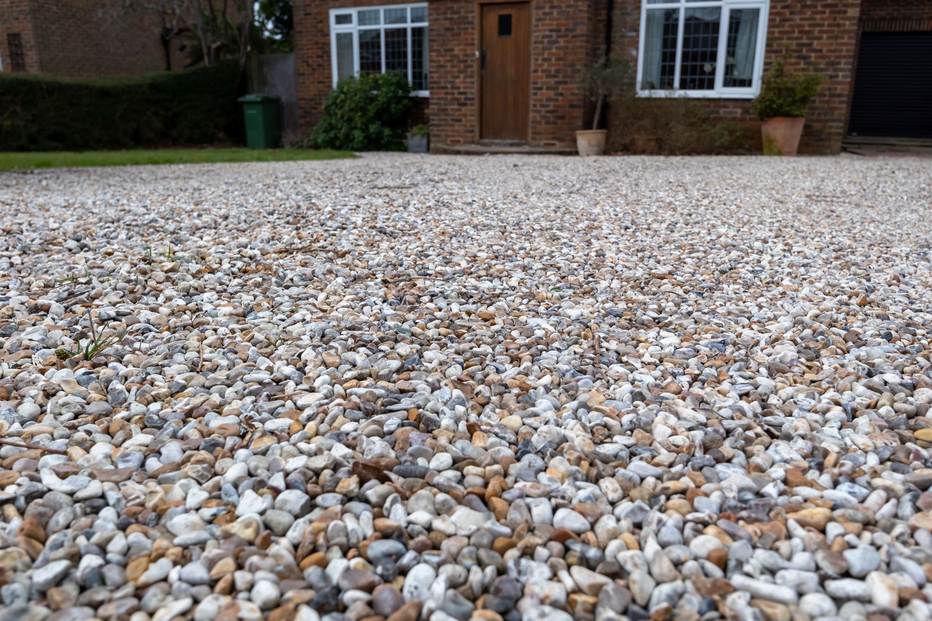 Gravel driveway in front of a brick house with a brown door and white-framed windows.