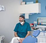 Un uomo che indossa una bandana e una mascherina è seduto su una poltrona del dentista
