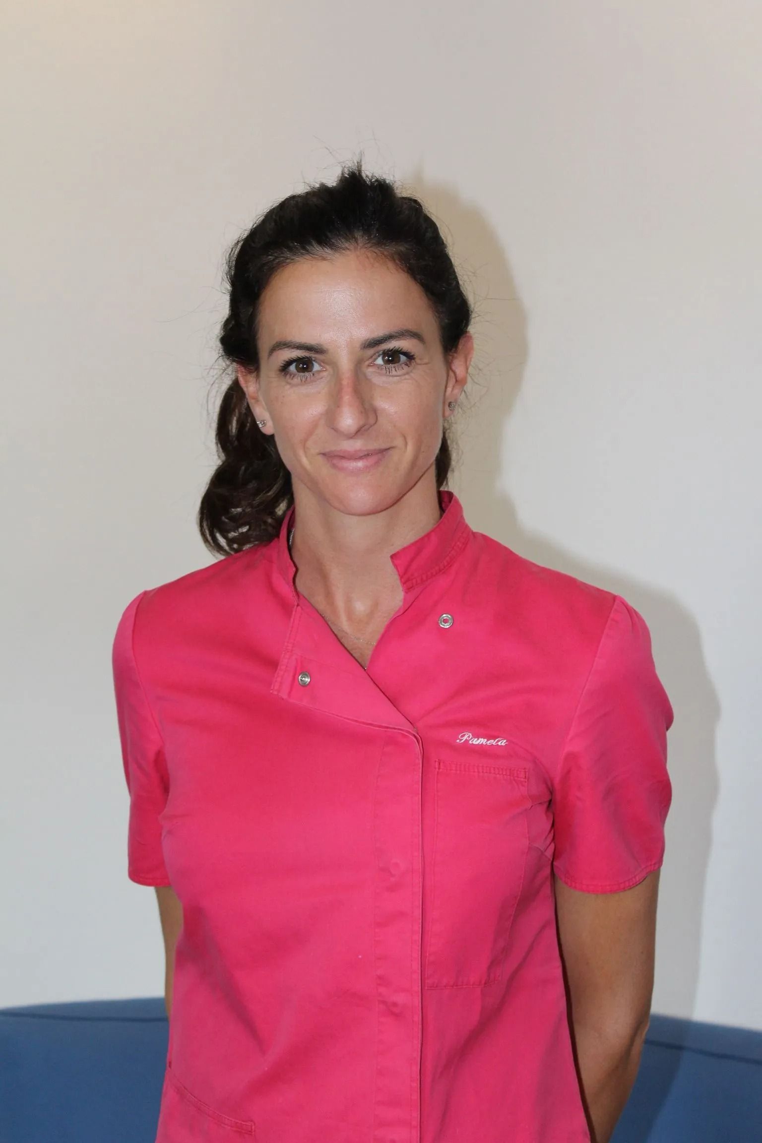 Una donna con una maglietta rosa è in piedi davanti a un muro bianco.