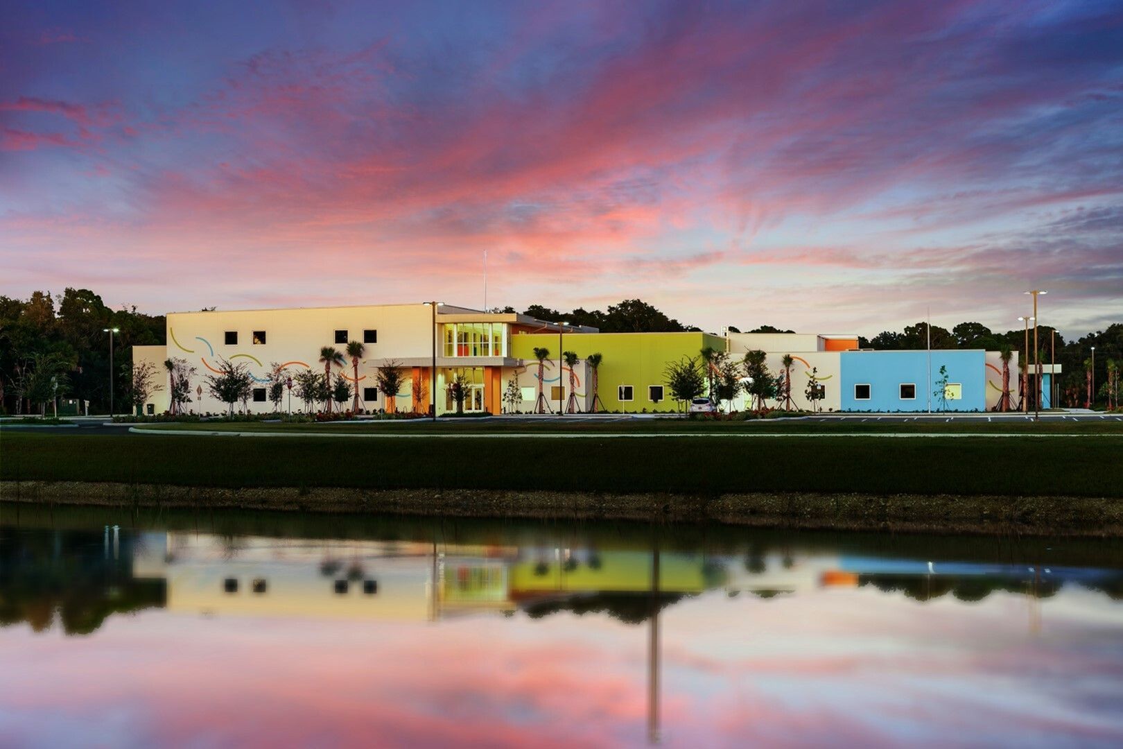 Colorful waterfront building at sunset, reflected in calm water under a pink-blue sky.