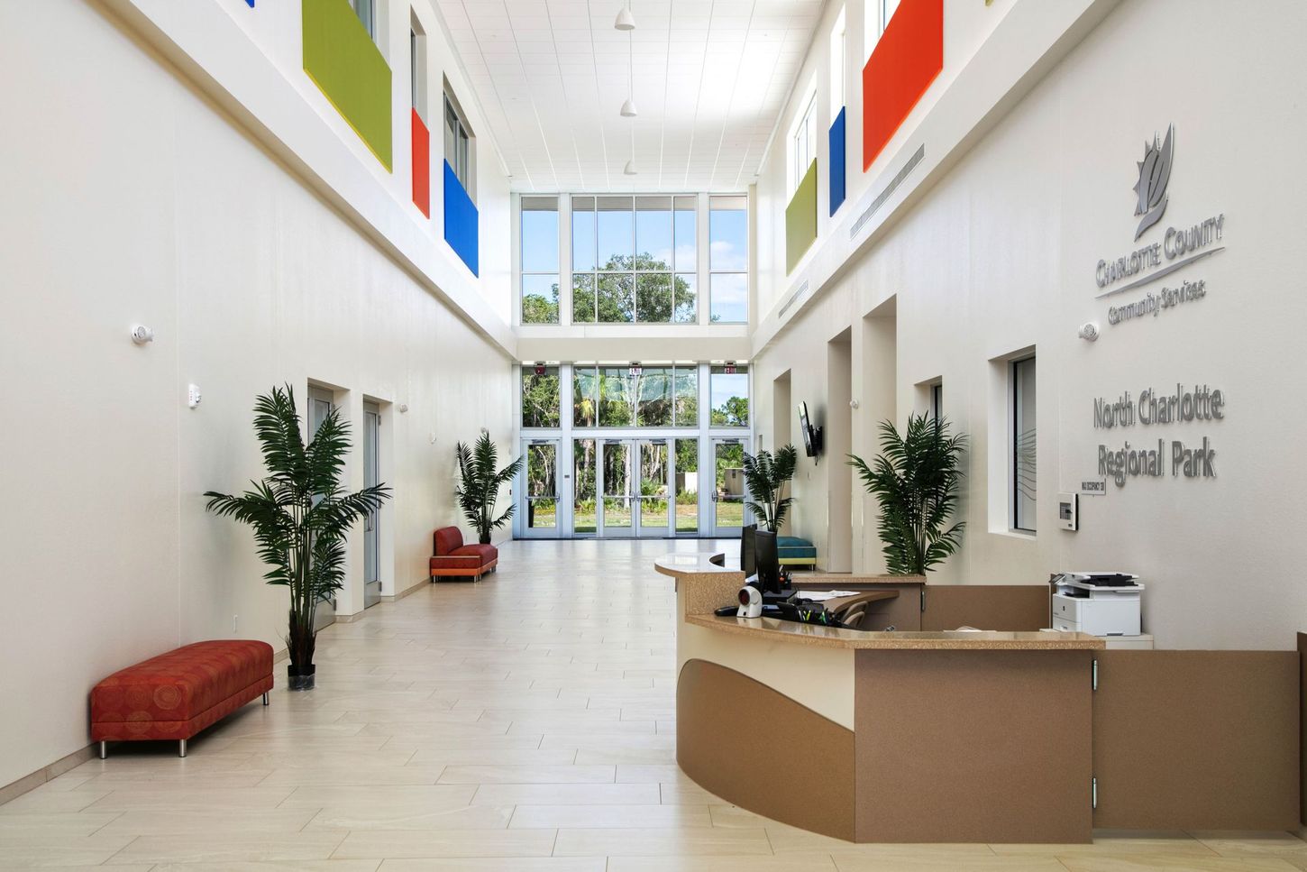 Bright modern lobby with reception desk, seating, plants, and tall windows under colorful wall panels