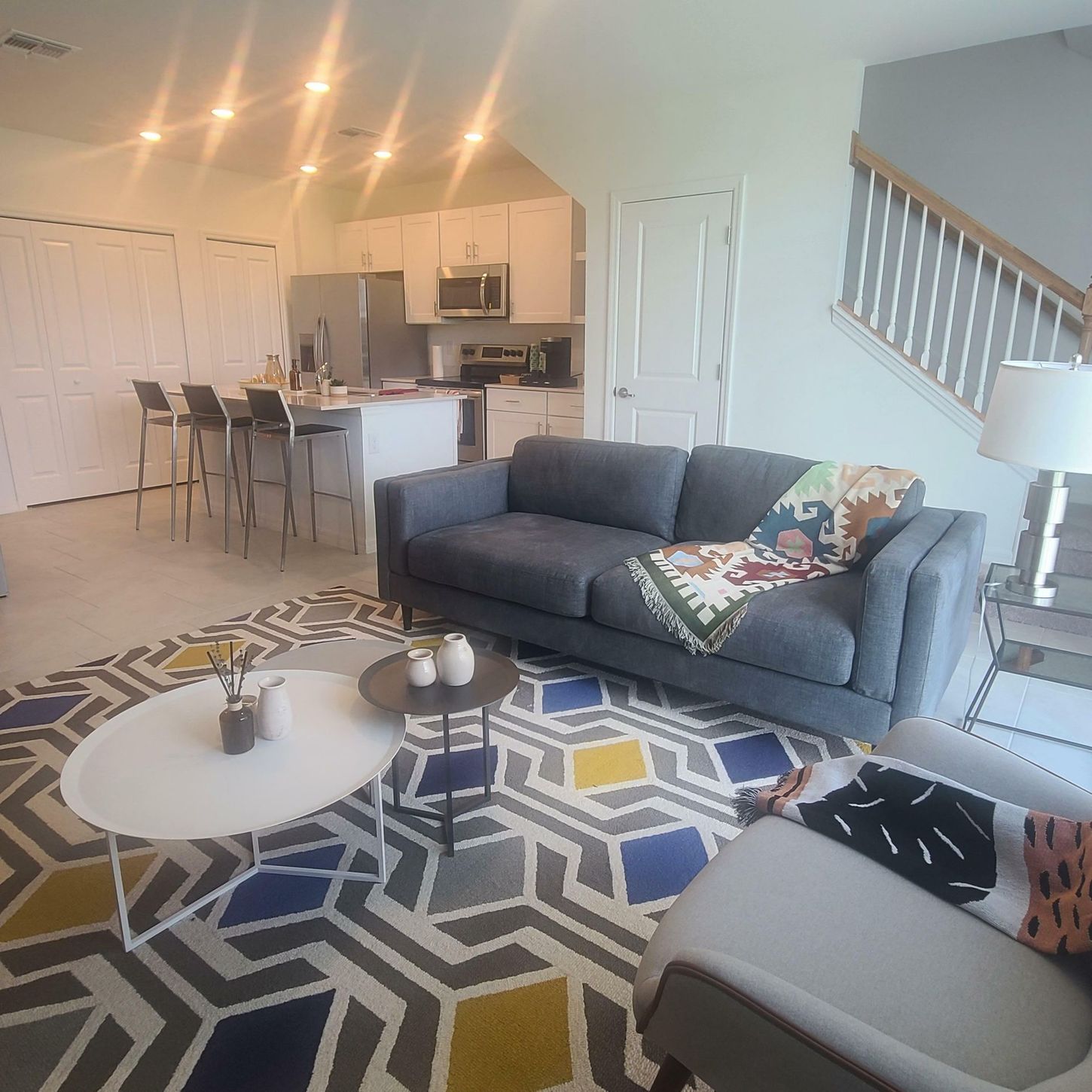 Bright living room with gray sofas, geometric rug, coffee table, and open kitchen with bar stools.