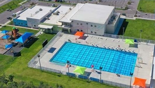 Aerial view of an outdoor swimming pool with a few colorful shade tents beside a large building