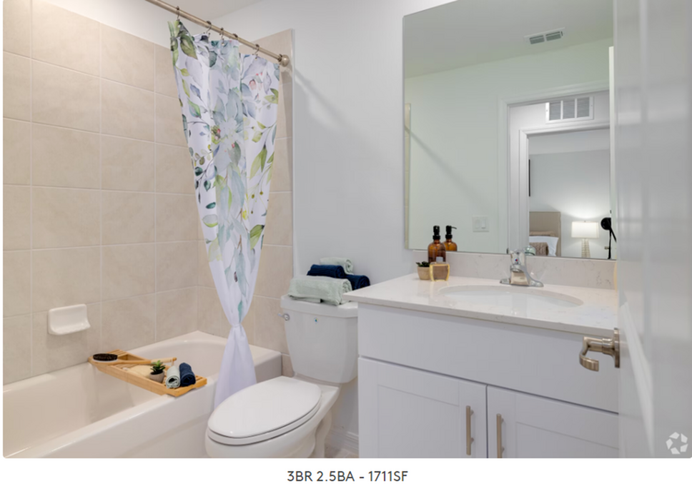 Bright bathroom with tub, floral shower curtain, vanity mirror, and white sink cabinet