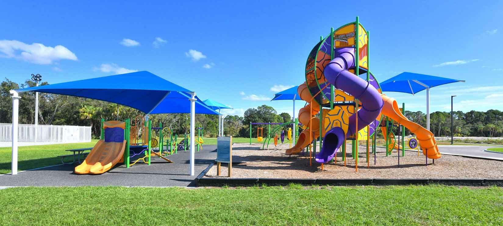 Colorful playground with slides, climbing structure, and blue shade canopies in a grassy park