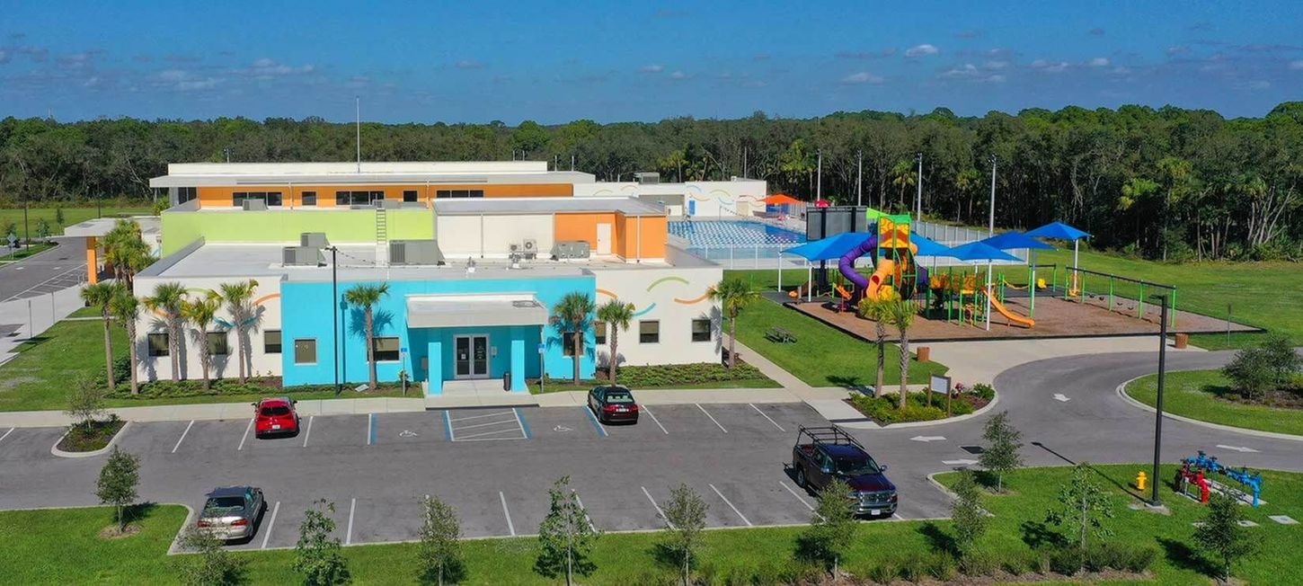 Aerial view of a colorful school building with a playground, parking lot, and cars on a sunny day
