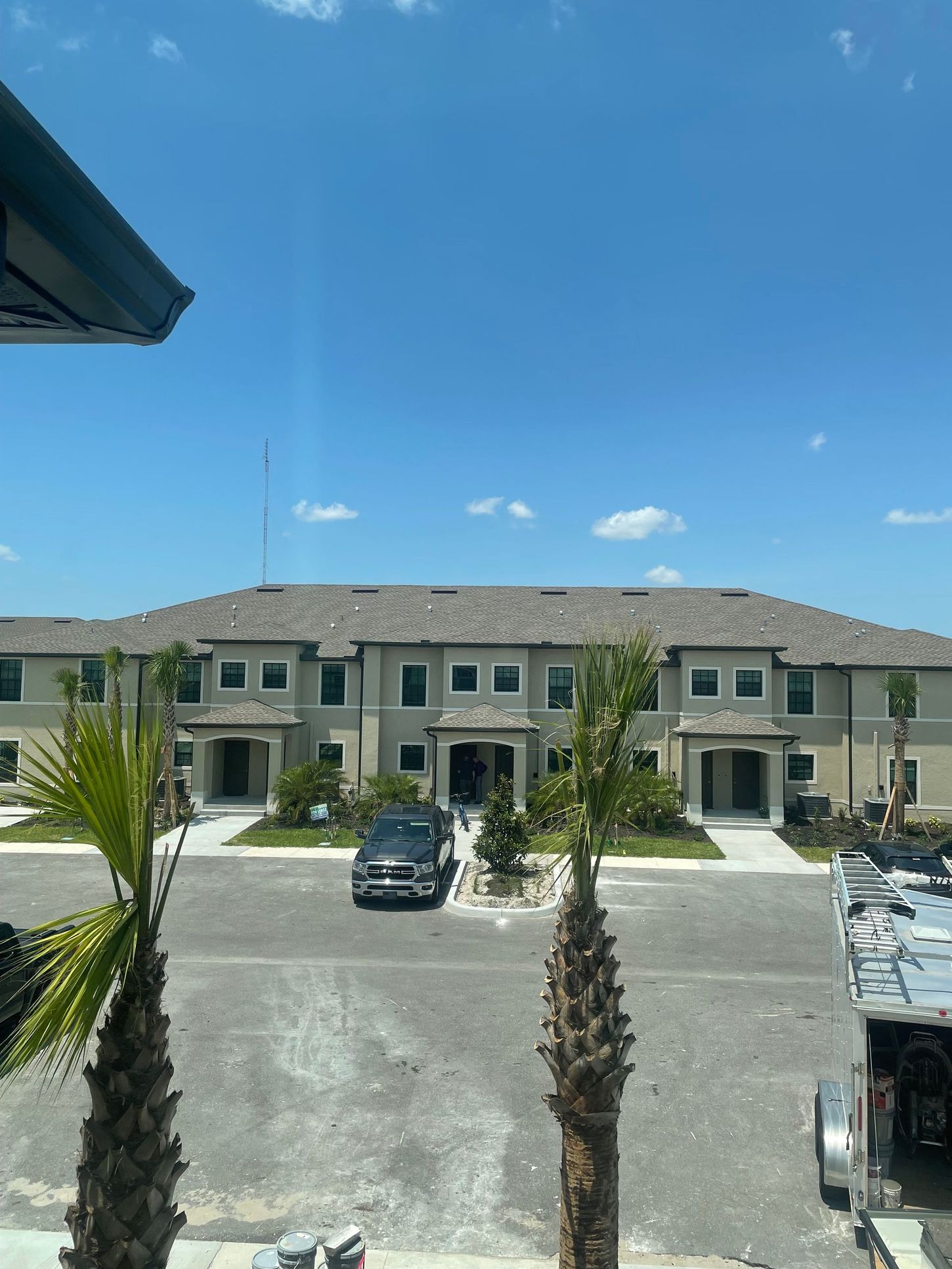 Apartment building with parked cars under a bright blue sky, viewed from a balcony
