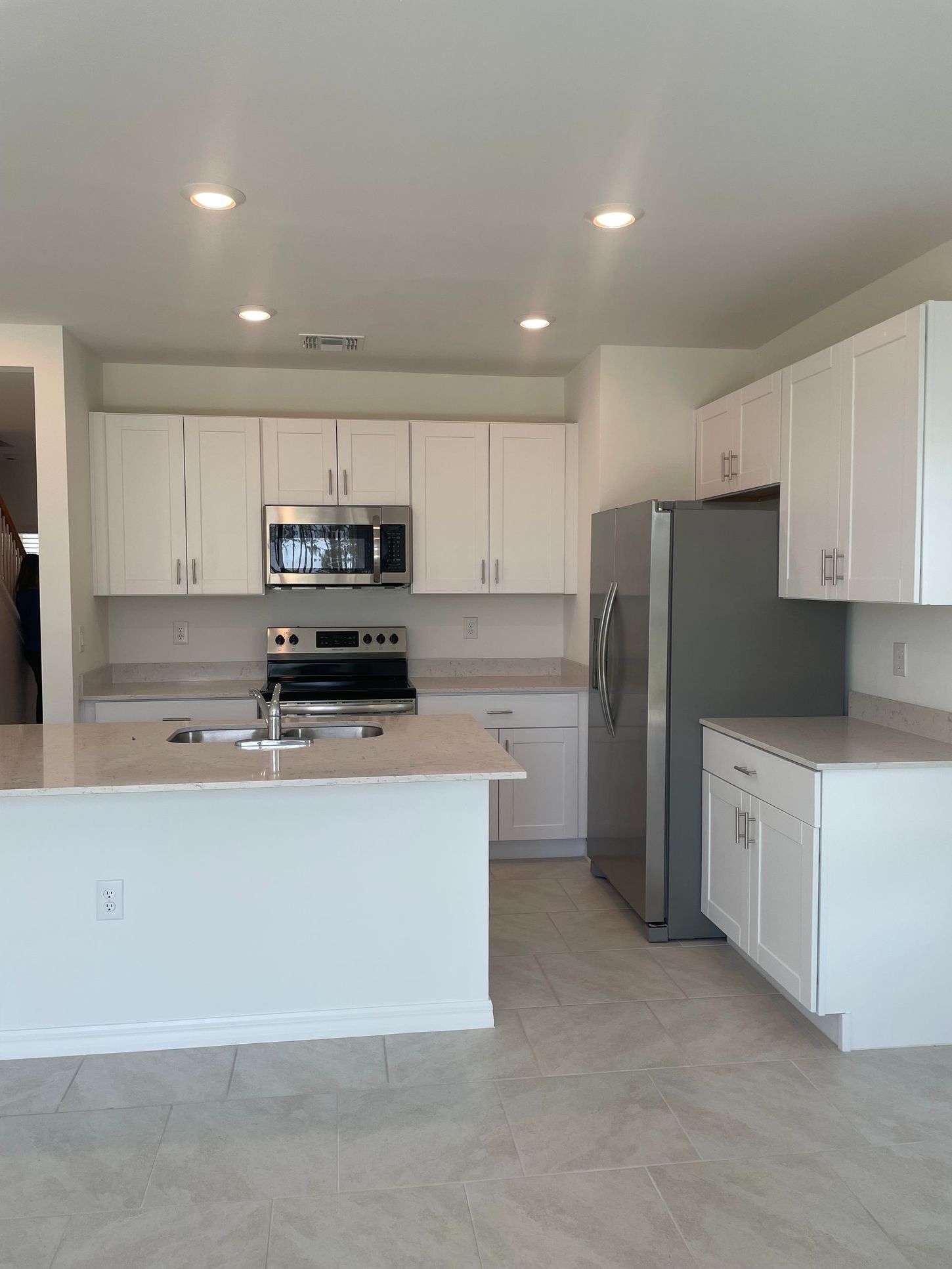 Bright modern white kitchen with island, stainless steel appliances, and recessed ceiling lights
