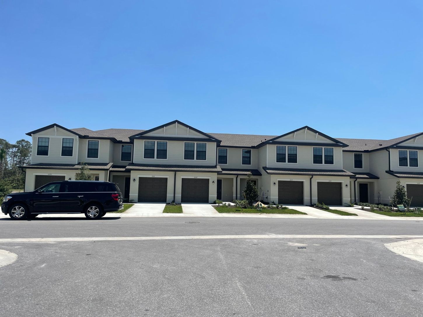 Row of modern townhomes with a black SUV parked in front under a clear blue sky