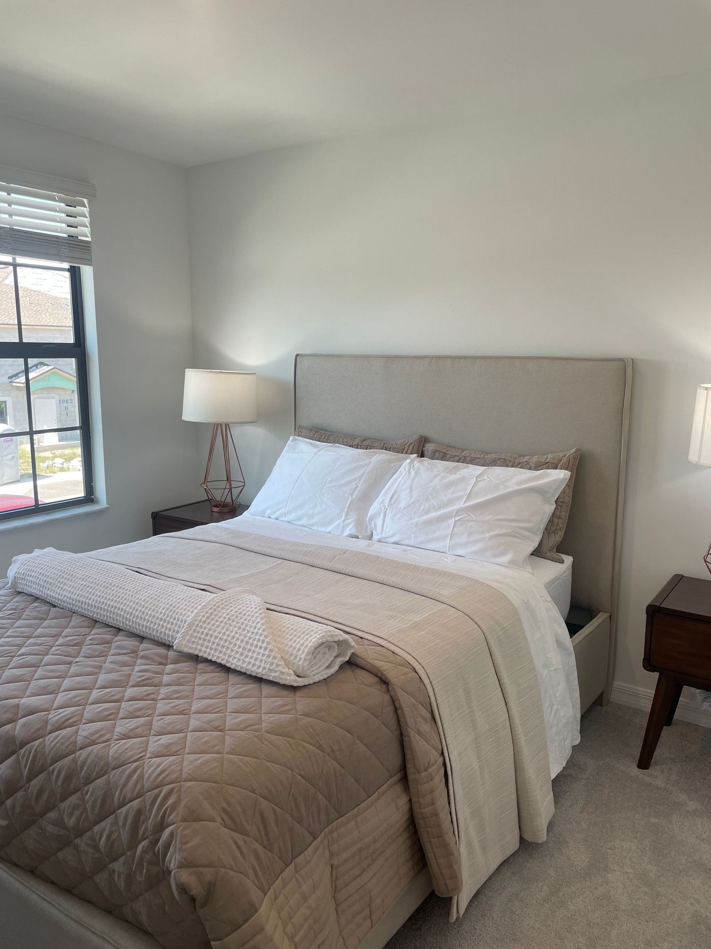 Neatly made bed with gray quilt, white pillows, and bedside lamp in a bright bedroom
