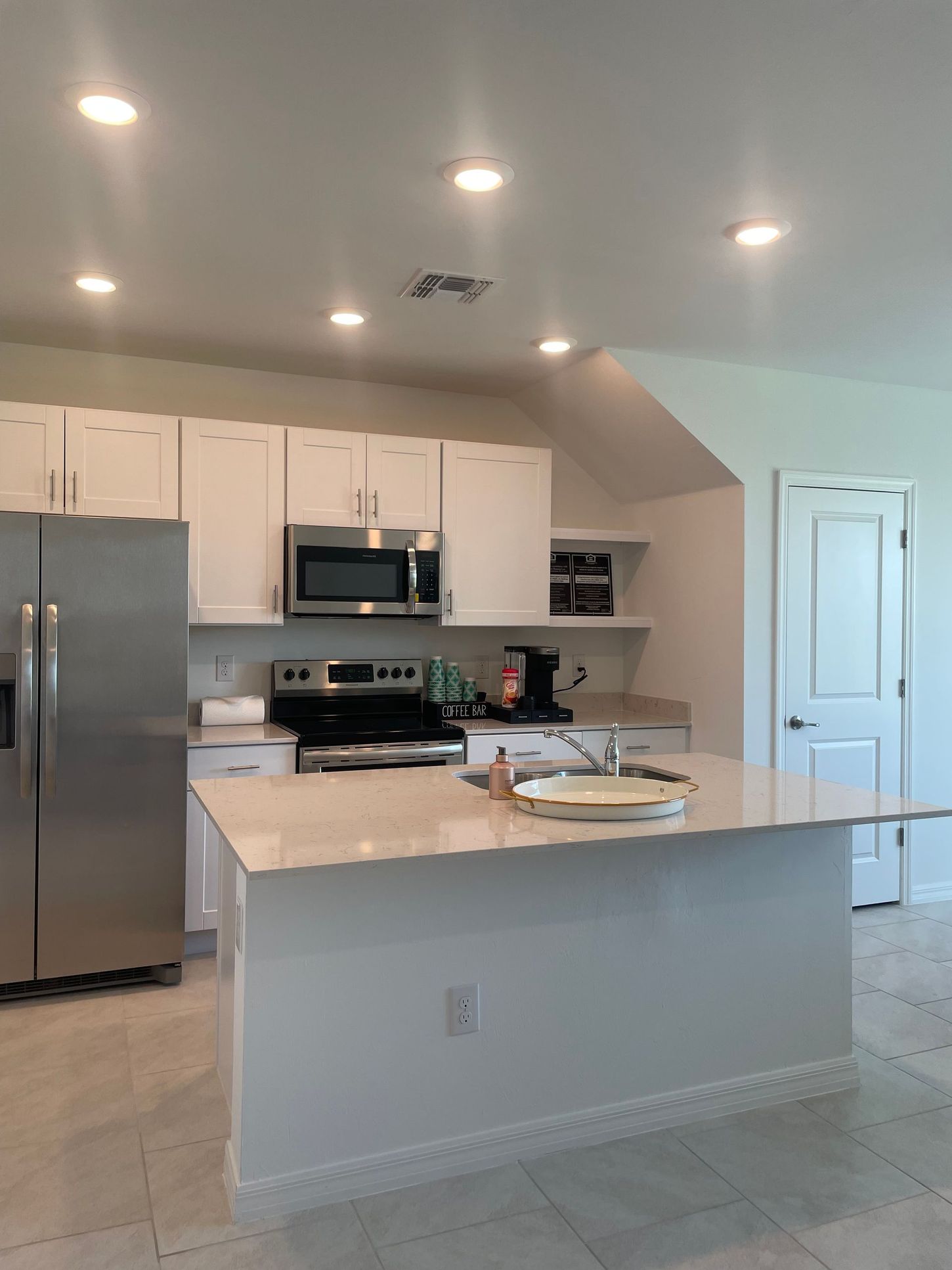 Bright modern kitchen with stainless appliances, white cabinets, and an island with a fruit bowl.