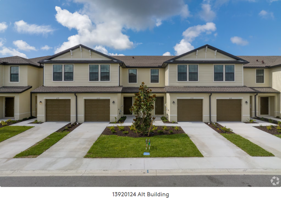 Row of beige townhouses with attached garages, driveways, and small front lawns under a blue sky