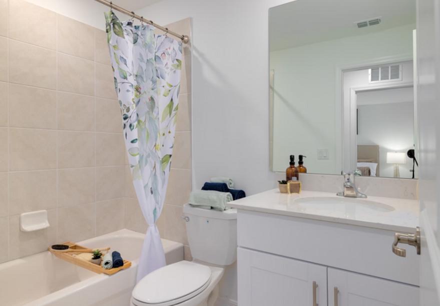 Bright bathroom with white vanity, mirror, toilet, bathtub, and floral shower curtain