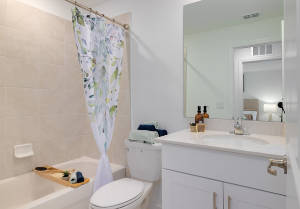 Bright bathroom with white vanity, mirror, toilet, bathtub, and floral shower curtain