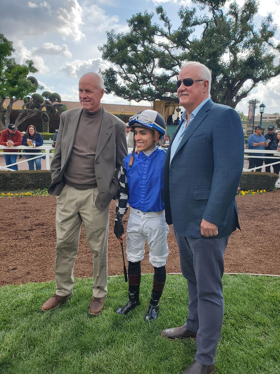 A jockey is posing for a picture with two men.