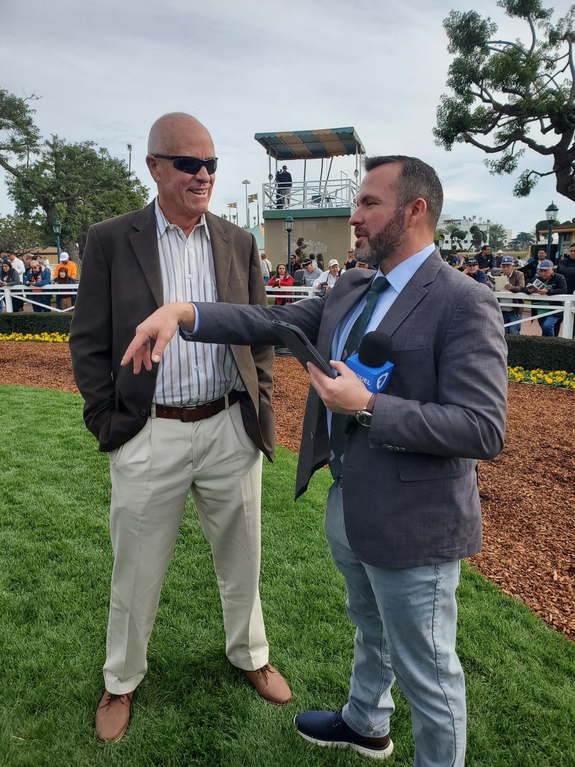 A man in a suit is talking to another man in a field