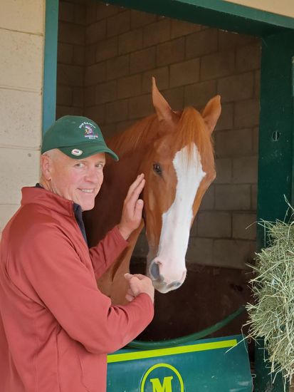 A man petting a horse in a stable with the letter m on the door