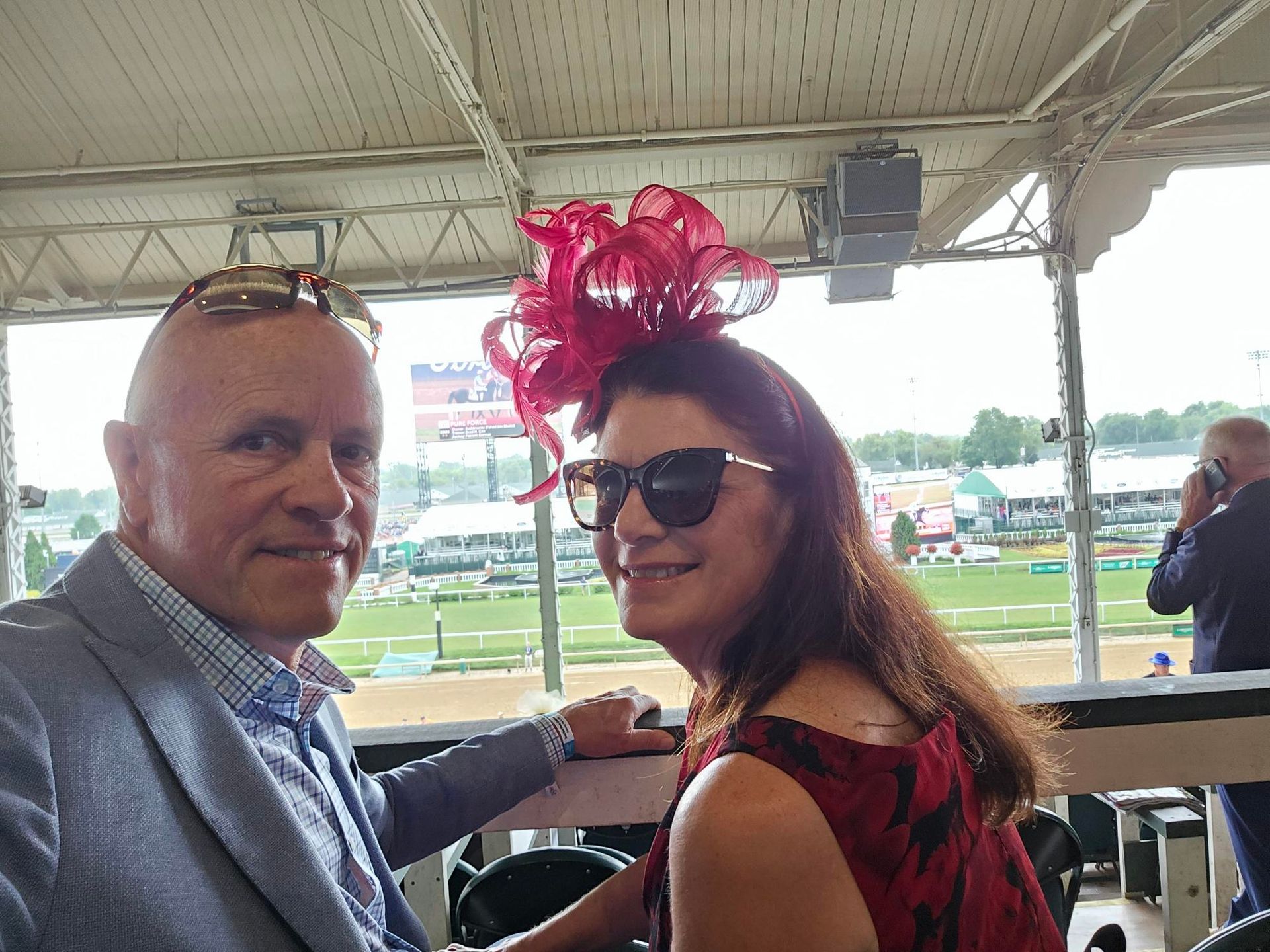 A man and a woman are sitting at a table at a race track . the woman is wearing a red hat.