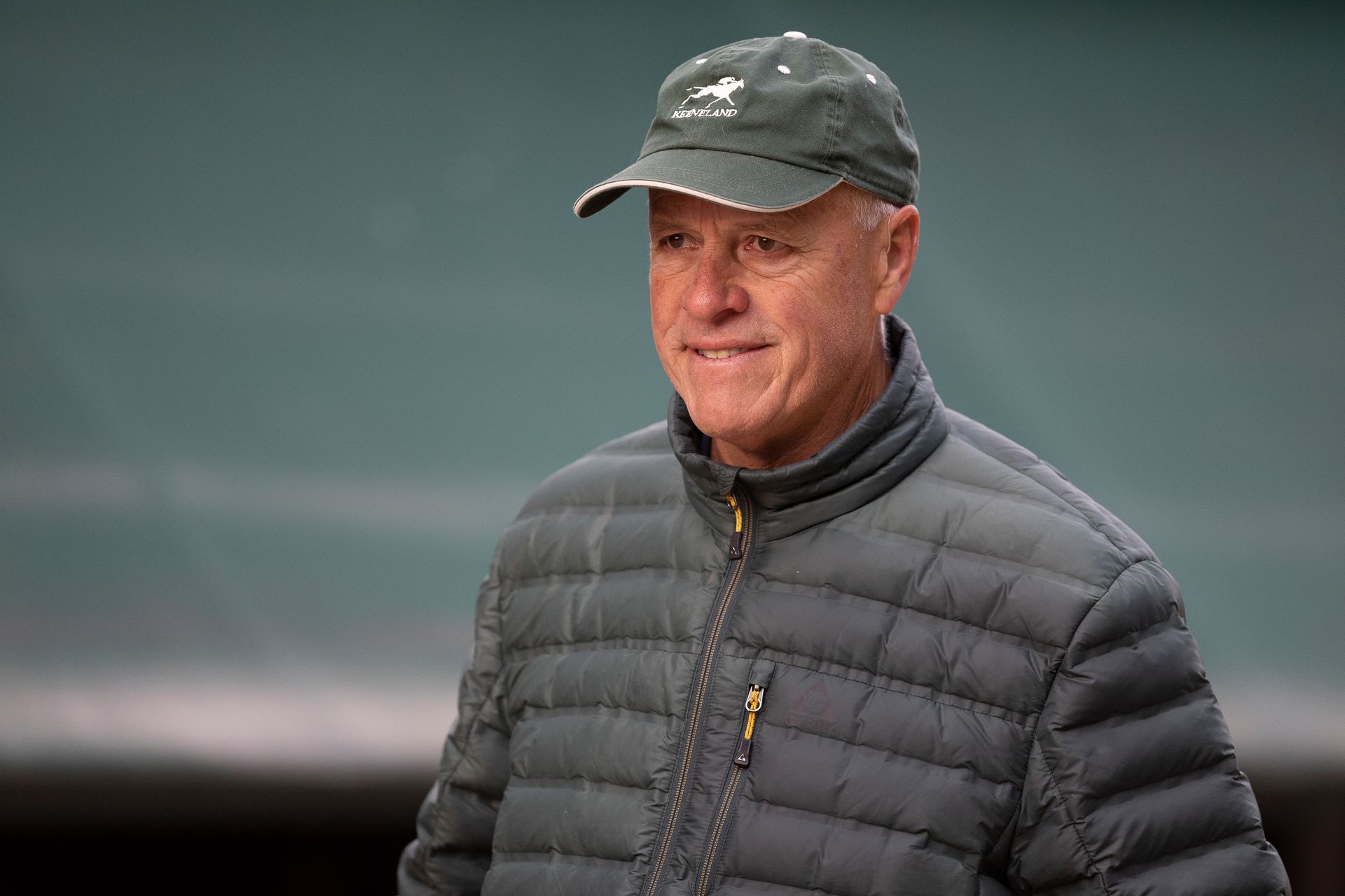 A man wearing a hat and a jacket is standing in front of a blue wall.