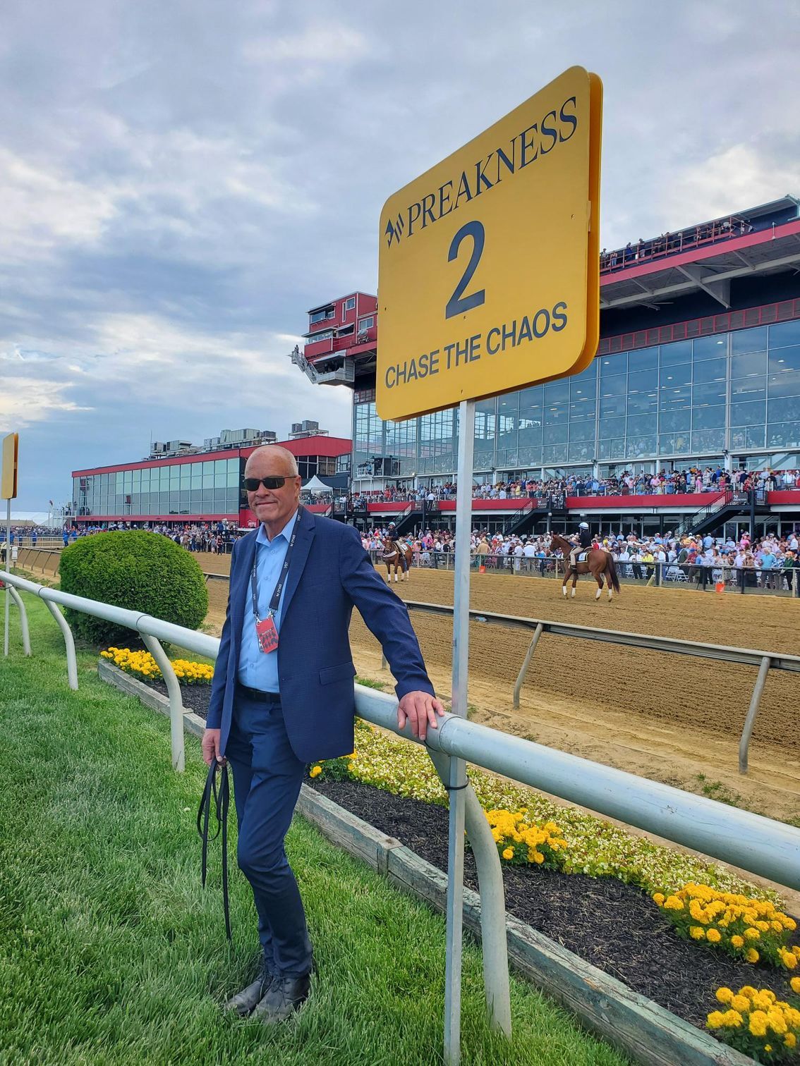 A man in a suit is leaning against a railing at a race track.