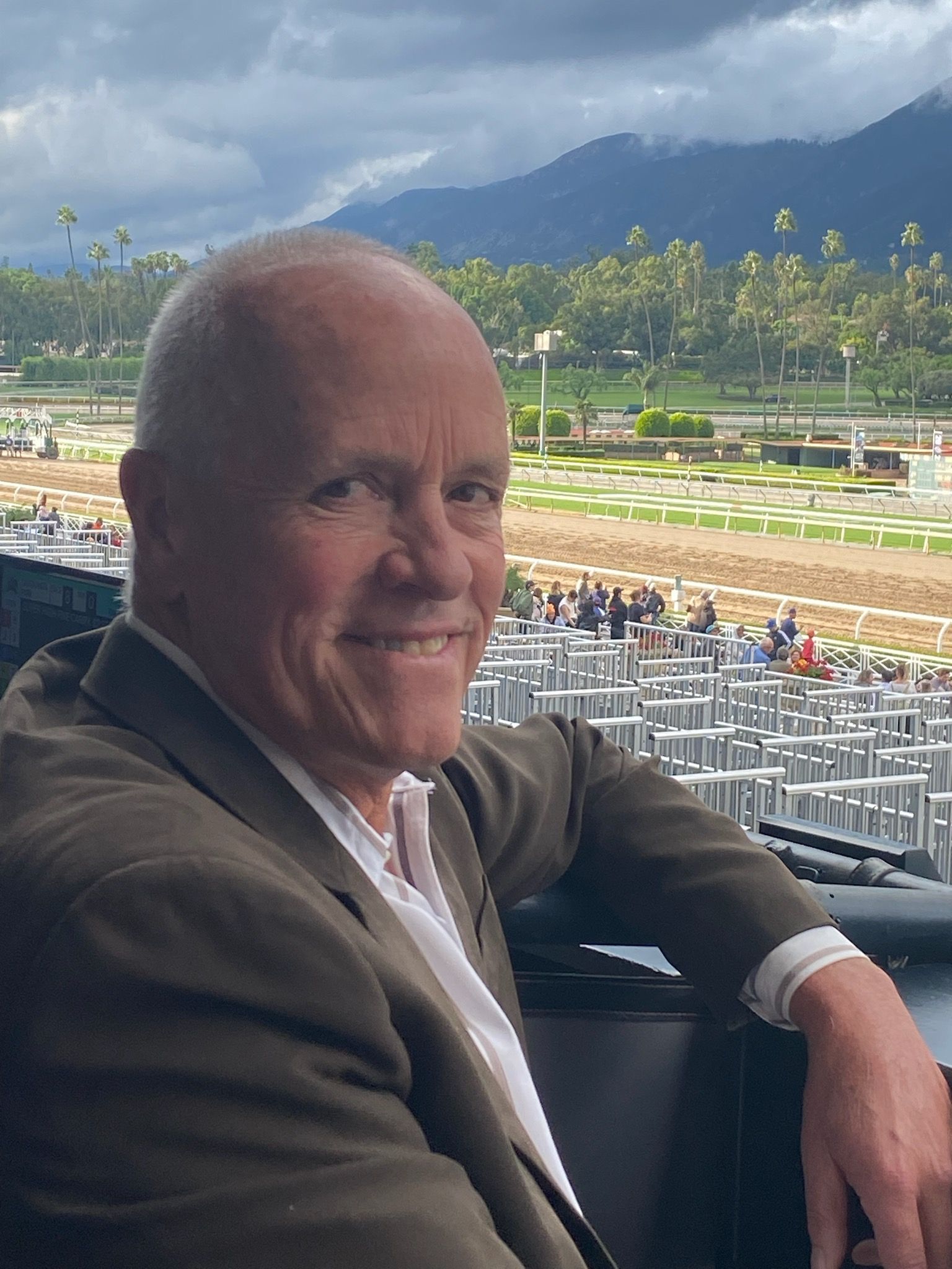 A man in a suit is sitting in a stadium with a view of a race track.