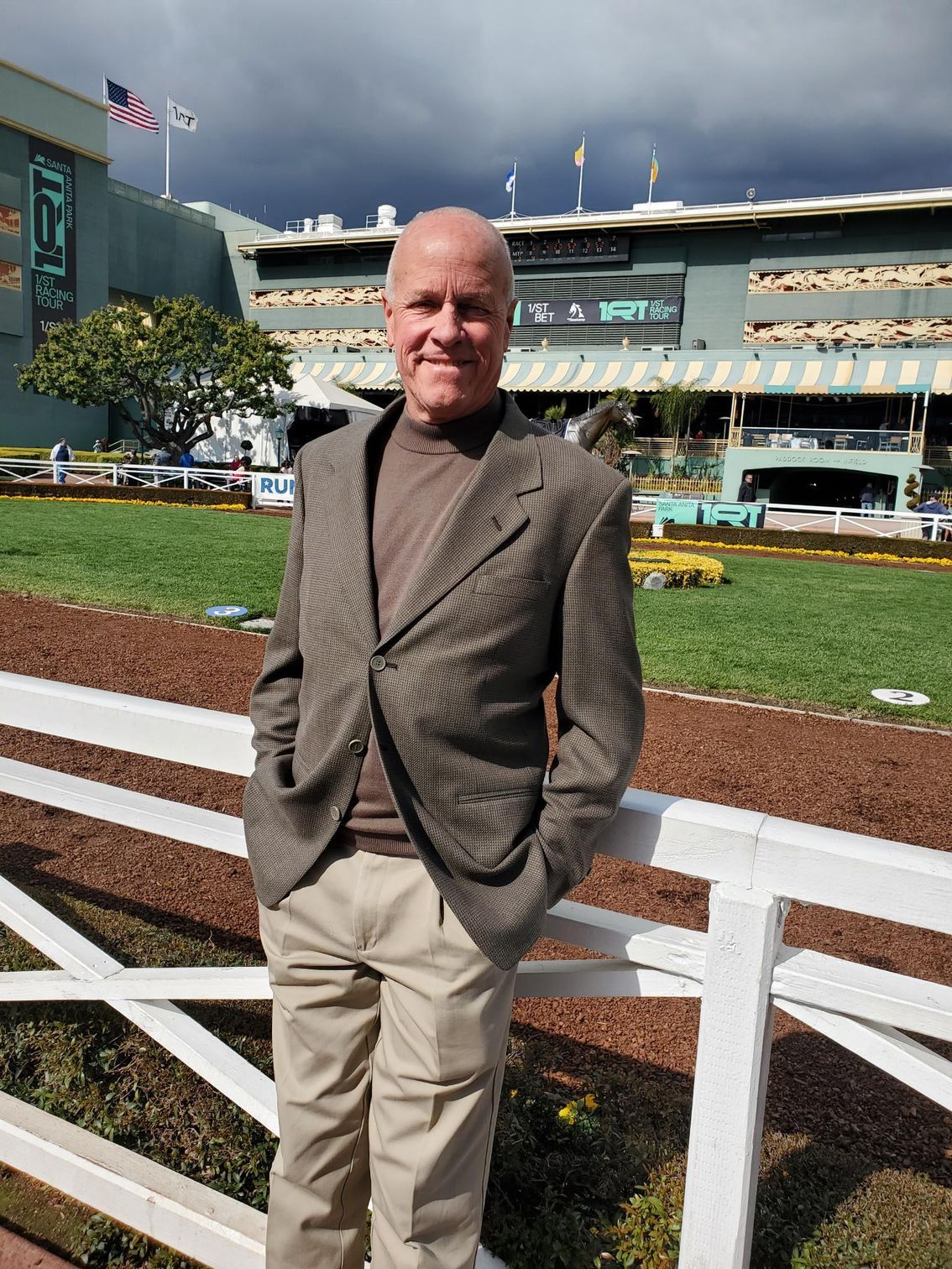 A man in a suit leans against a white fence