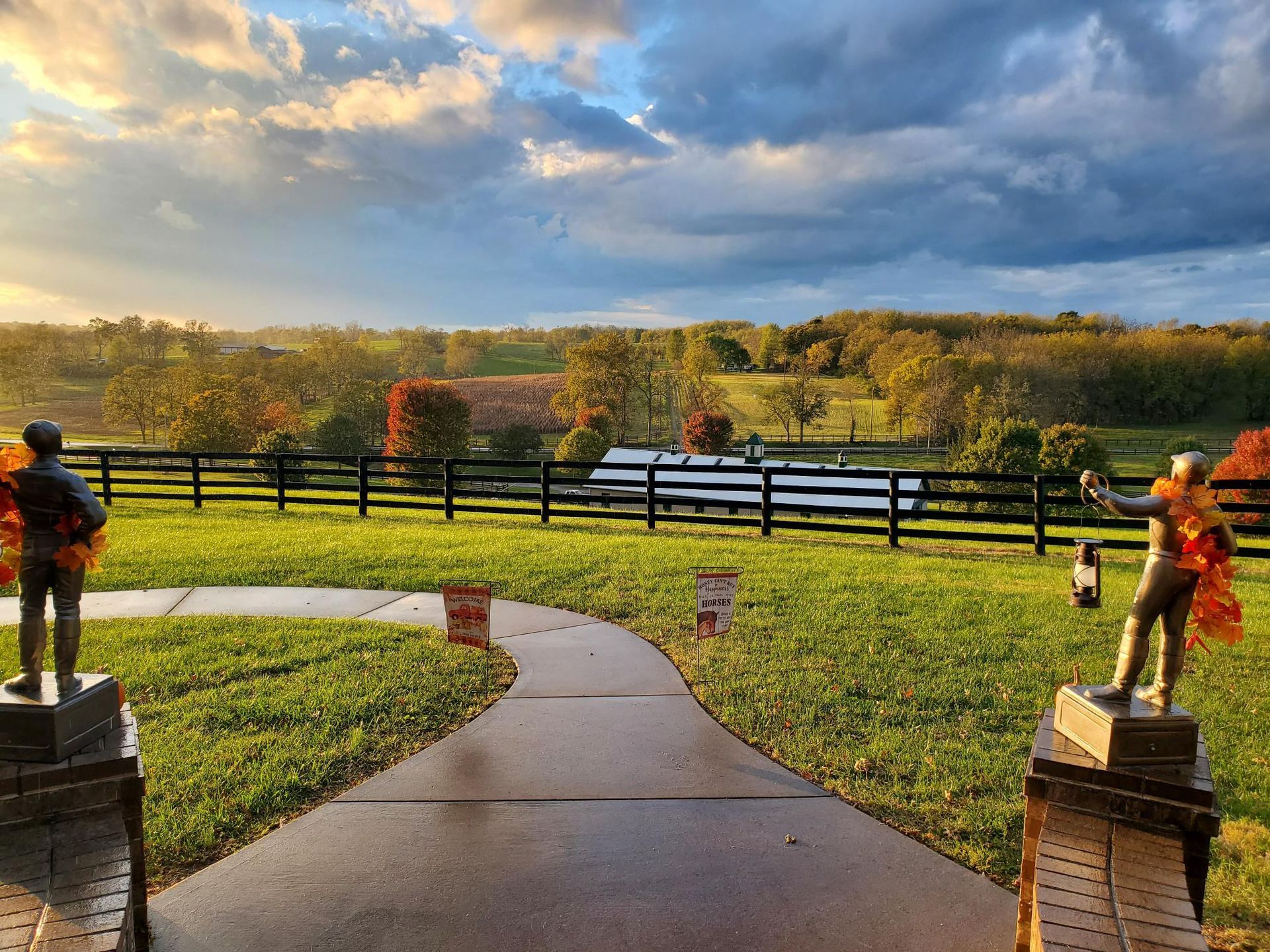 A path leading to a fenced in field with two statues on the side of it.