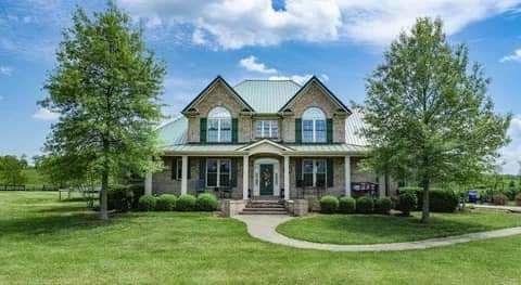 A large house with a green roof is sitting on top of a lush green field.