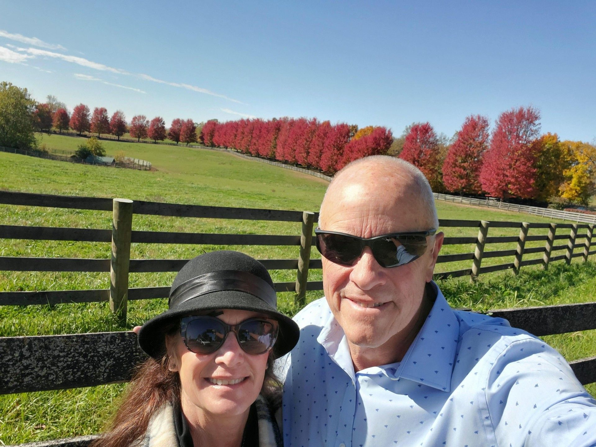 A man and a woman are posing for a selfie in front of a fence in a field.