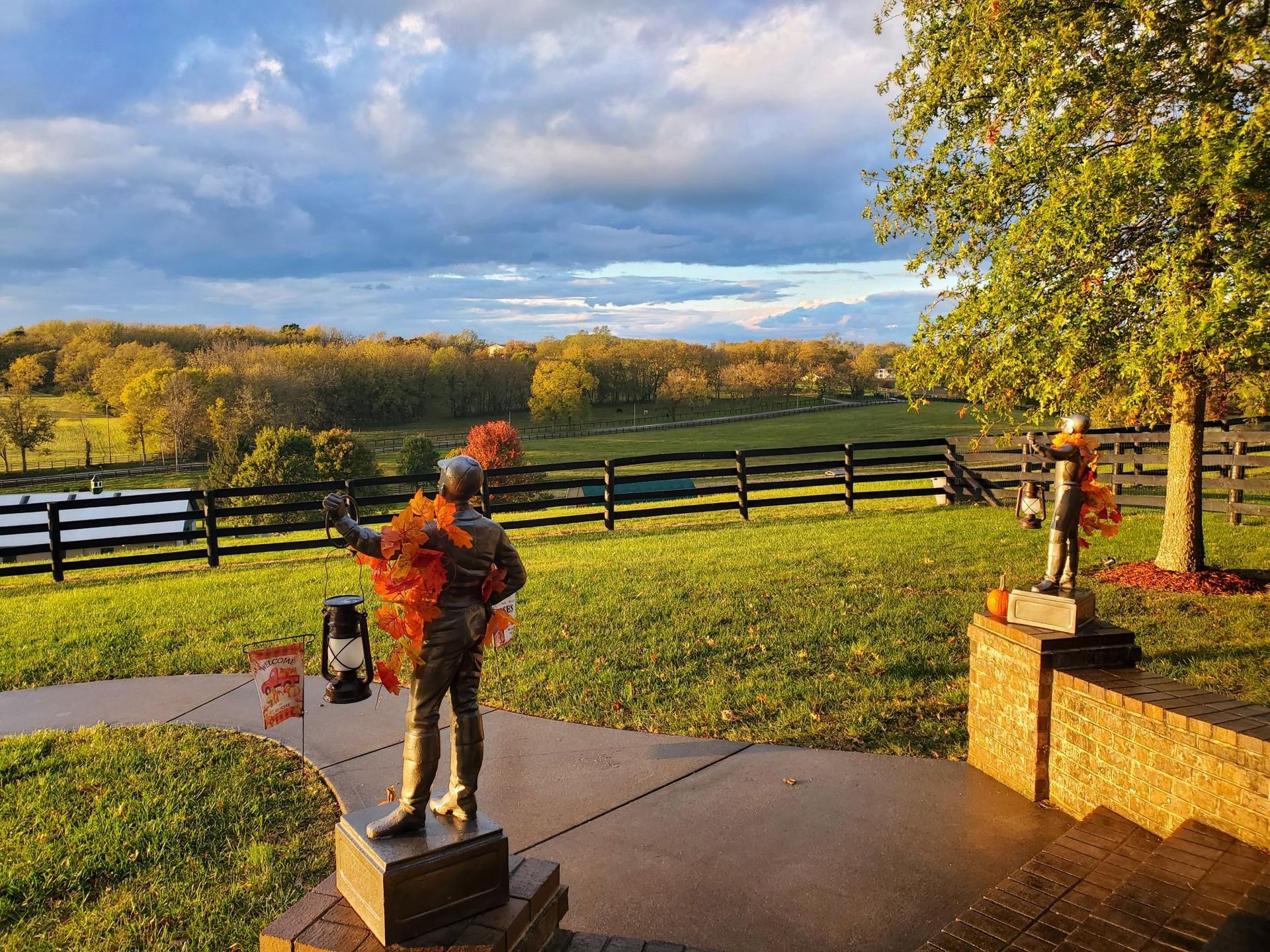A statue of a man holding a lantern in a field with a fence in the background.